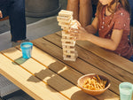 Neighbor Haven Square Coffee Table with concrete top in outdoor setting, with family playing Jenga, striped wood chairs nearby, sunny ambiance