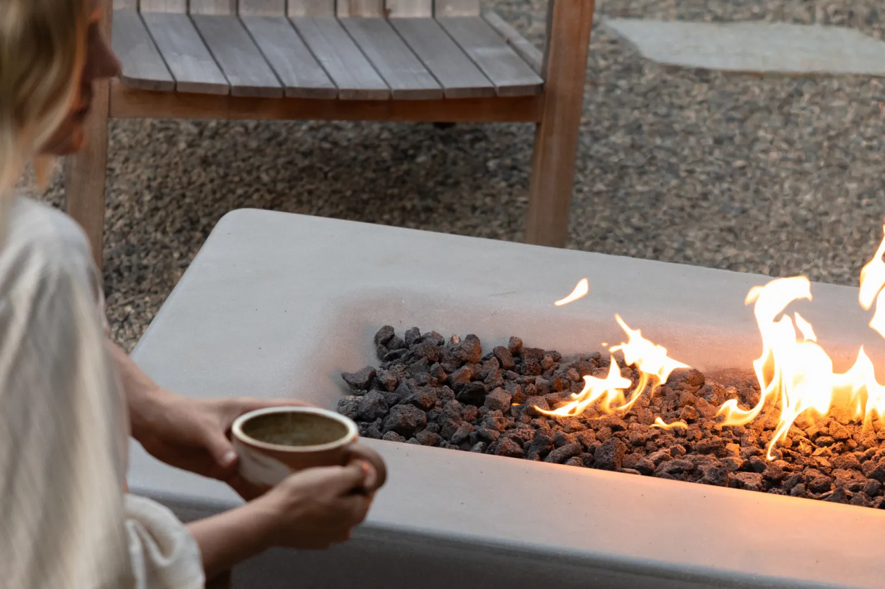 Taylr Anne Castro holds a mug of matcha while sitting beside the fire table, with her son nearby