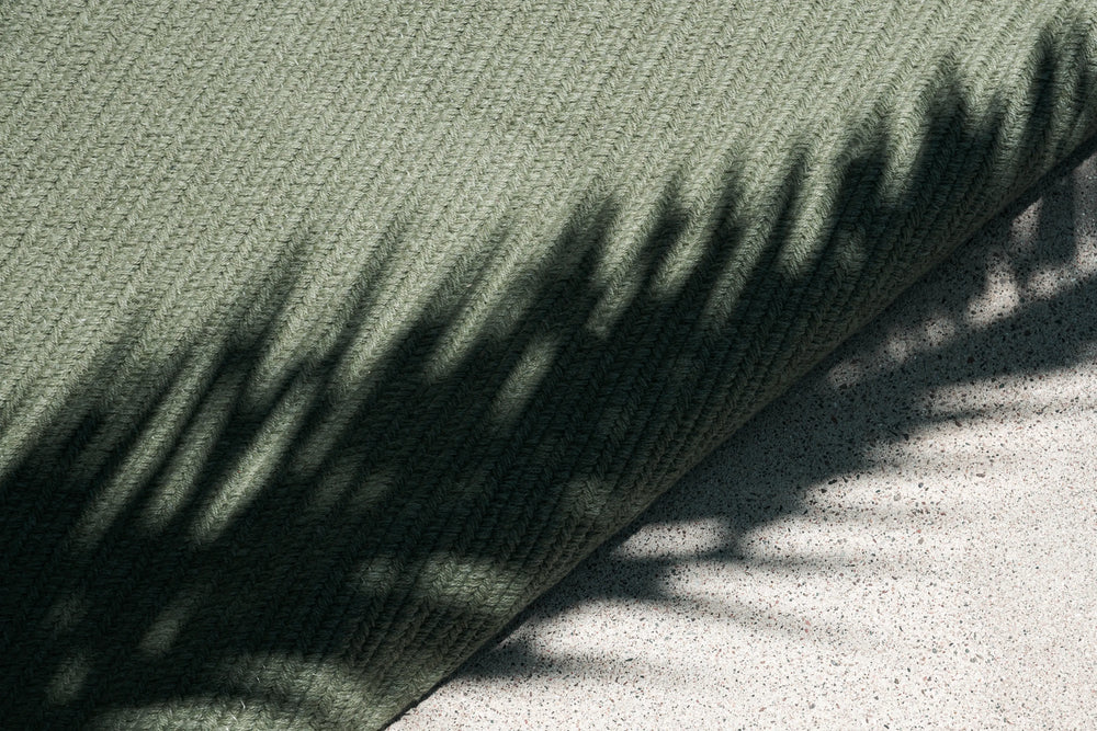 Neighbor Braid Rug in Basil colorway detail, striped diagonal pattern with plant shadows cast across green textured surface