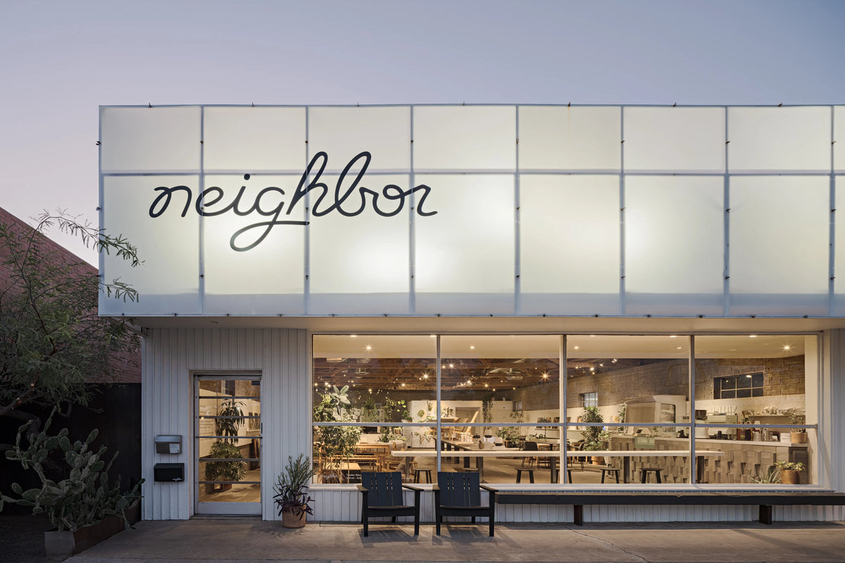 Neighbor showroom storefront at night with illuminated display windows, black outdoor chairs, modern facade