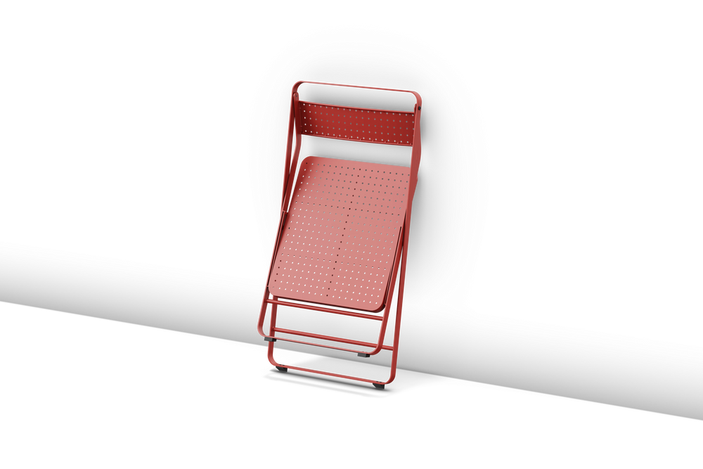 Neighbor Take Two Bistro Chair, an all-metal folding chair with perforated steel seat and backrest in coral red, shown fully folded for storage.