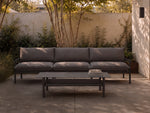 Neighbor Underline Coffee Table in charcoal, a low rectangular table on tubular legs with a recessed lower shelf, beside a sofa.