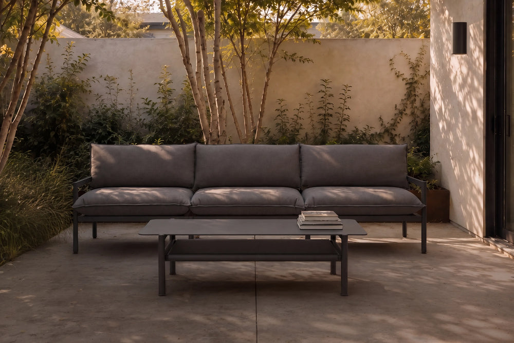 Neighbor Underline Coffee Table in charcoal, a low rectangular table on tubular legs with a recessed lower shelf, beside a sofa.