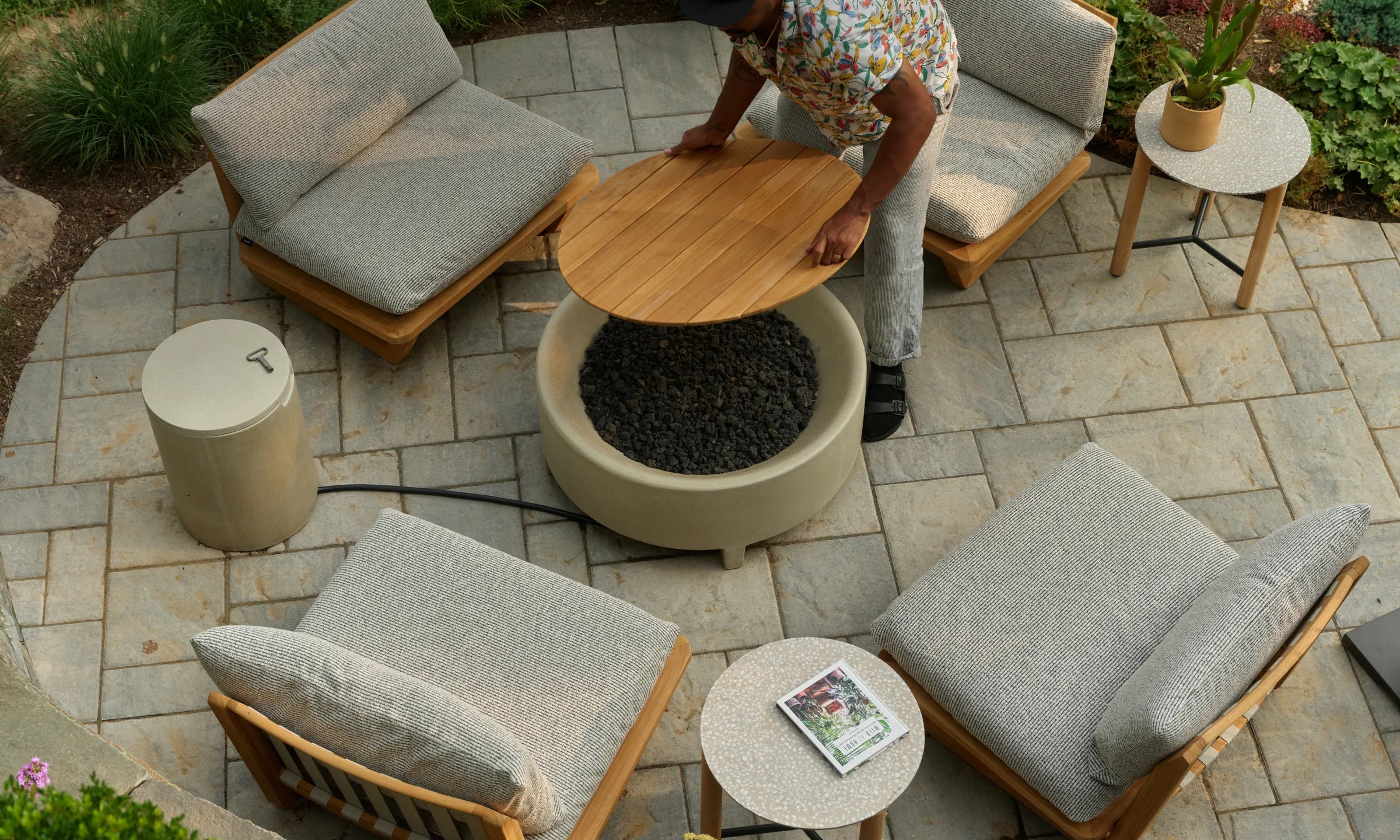 Overhead view of Hilton Carter's stone patio with a Rook fire table, two Dweller lounge chairs and a Haven round side table holding a magazine