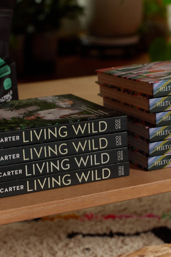 Stacks of Living Wild books by Hilton Carter on a wooden table above a patterned rug.