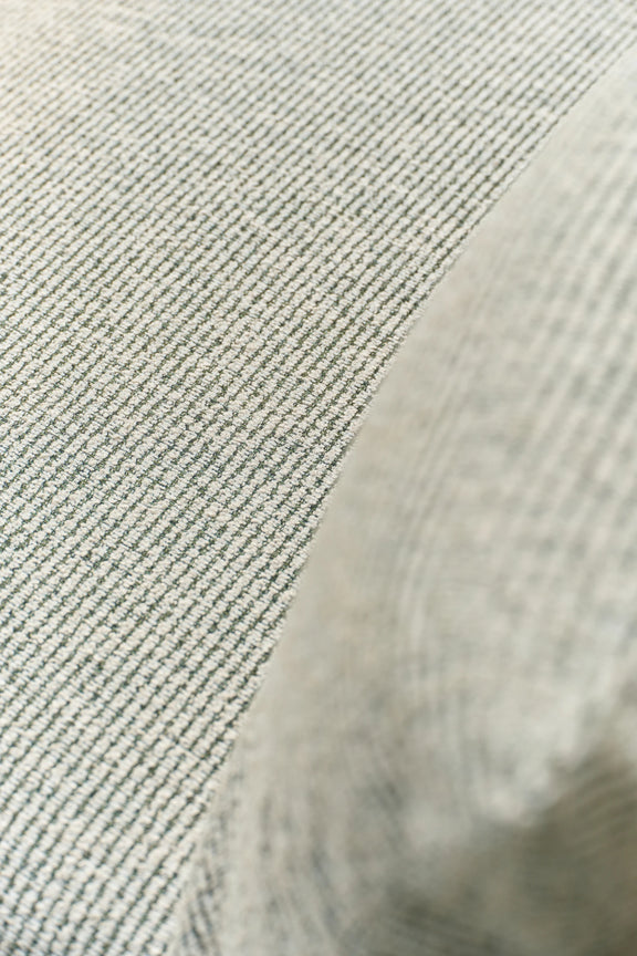 Close-up of woven gray-green outdoor fabric curving over a cushion edge.