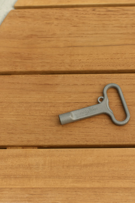 A gray metal furniture key lying on a teak tabletop.