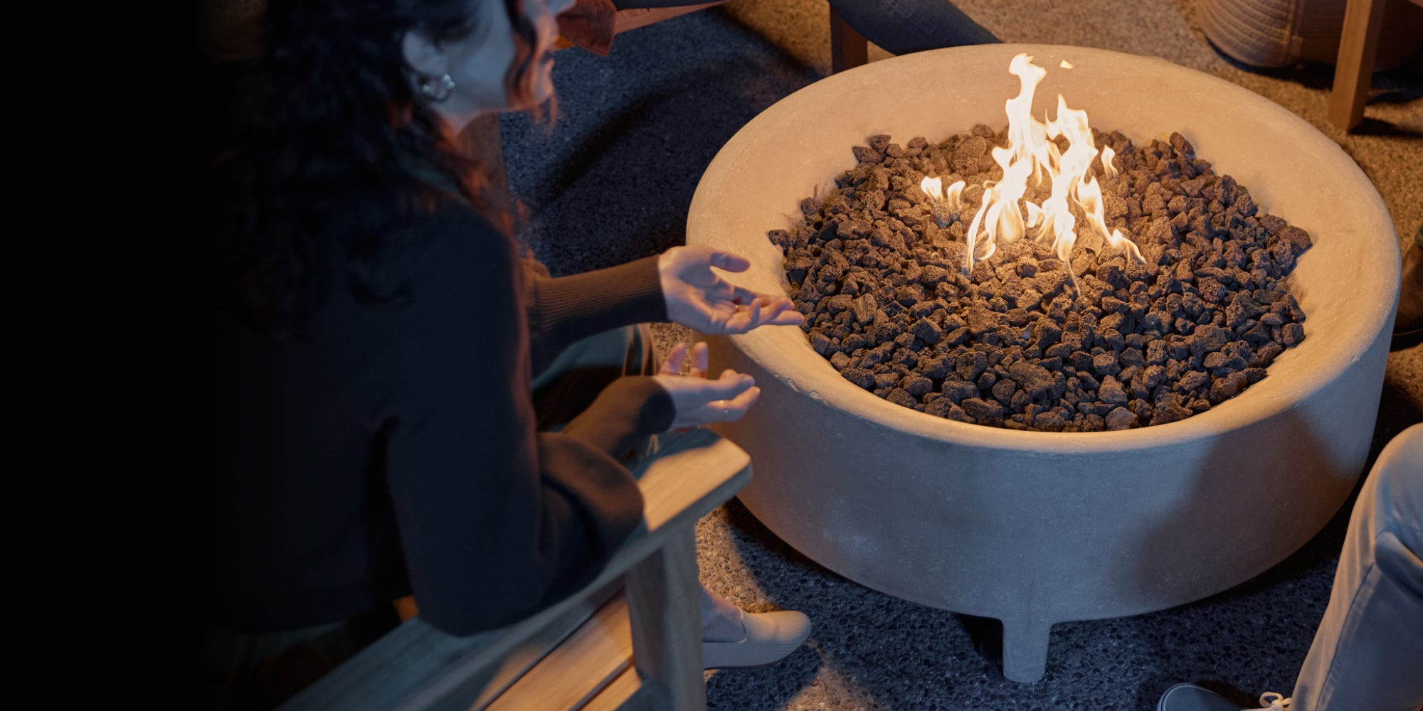 People gathered around a fire pit table with flames in a dimly lit patio