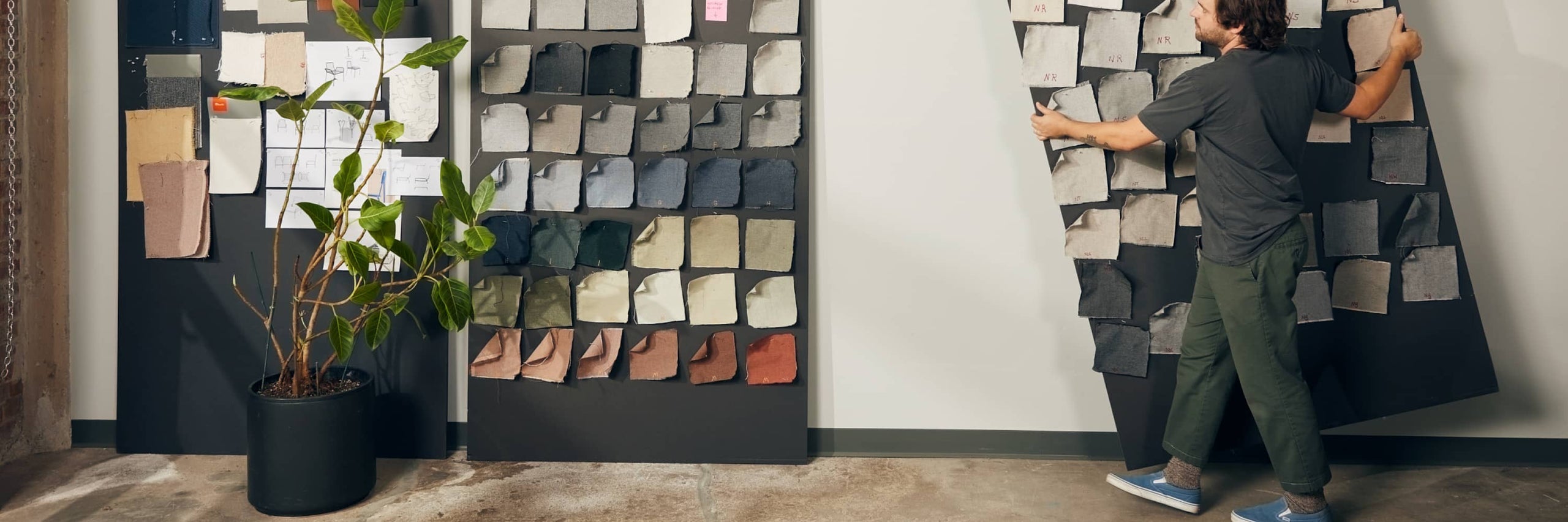 Designer arranging fabric and material swatches on a large display board in a studio