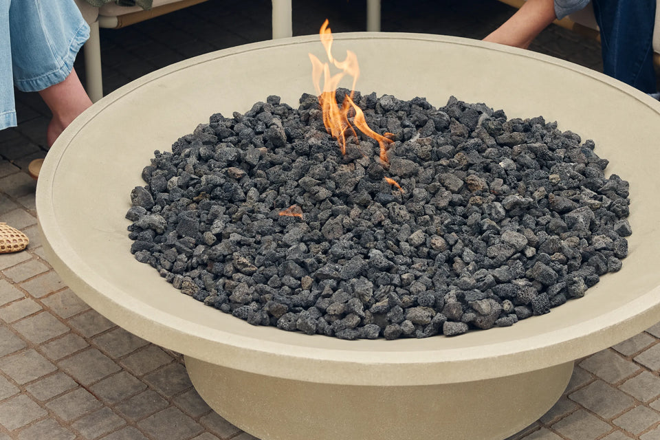 Closeup of Neighbor Brimfire table filled with lava rocks and open flame on a cobblestone patio, Neighbor Camber Sectional visible at edge