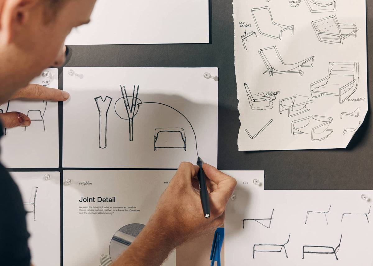 Designer reviewing furniture technical sketches and structural drawings spread across a work table