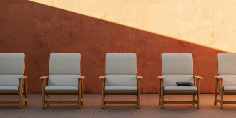 Five Neighbor Low Chairs with teak frames and cream cushions in a row against a terracotta stucco wall on brick pavers