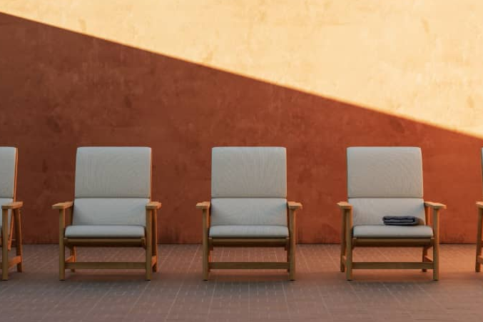 Five Neighbor Low Chairs with teak frames and cream cushions in a row against a terracotta stucco wall on brick pavers