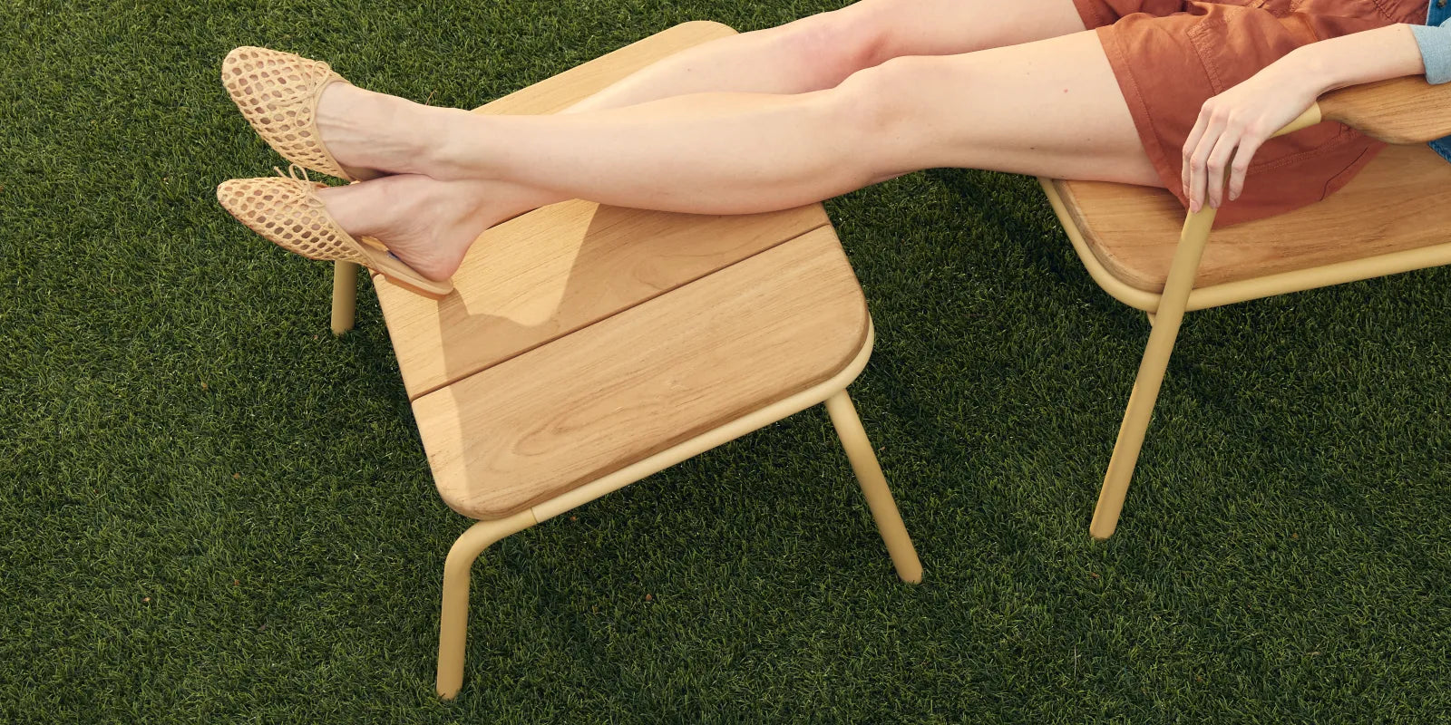 Hopper Ottoman with solid wood construction and curved metal frame, viewed from three-quarter angle on grass
