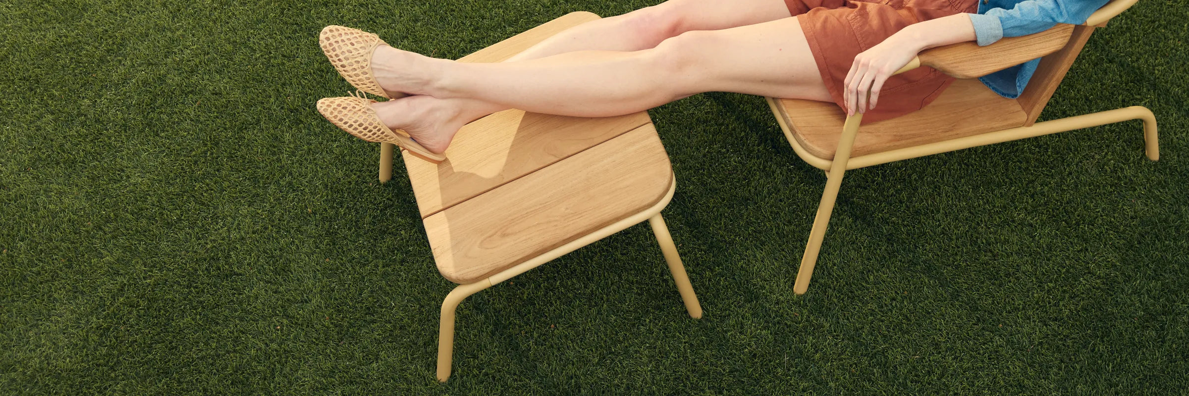 Hopper Ottoman with solid wood construction and curved metal frame, viewed from three-quarter angle on grass