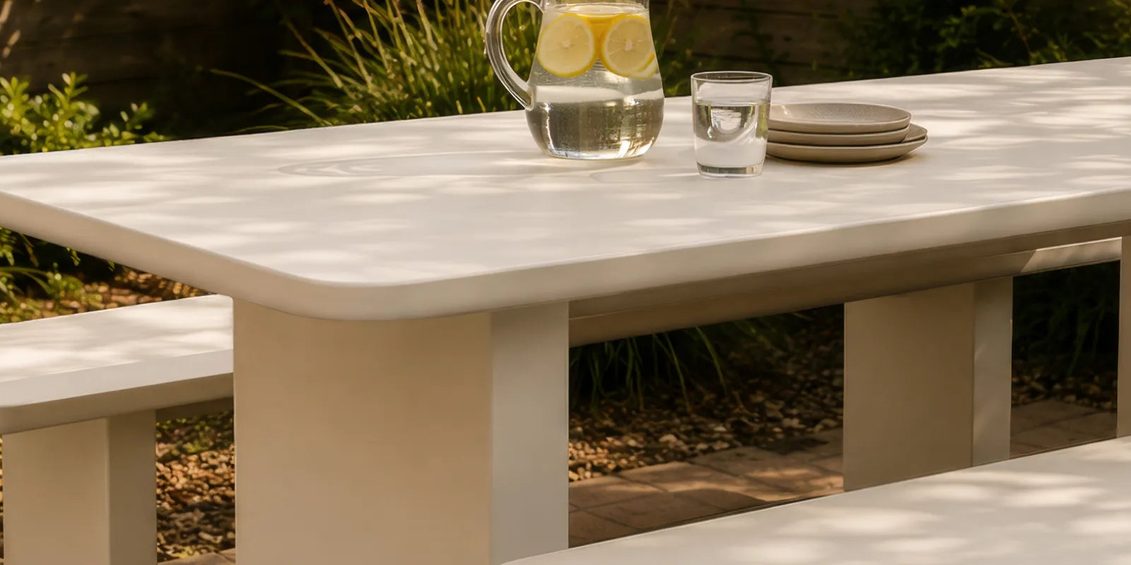 Angled view of the Massif Dining Set, an ivory concrete composite table with rounded corners and two integrated benches.