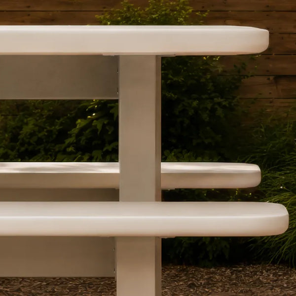 Massif dining table edge and integrated bench in ivory concrete composite, with thick rounded profiles and a slab leg.