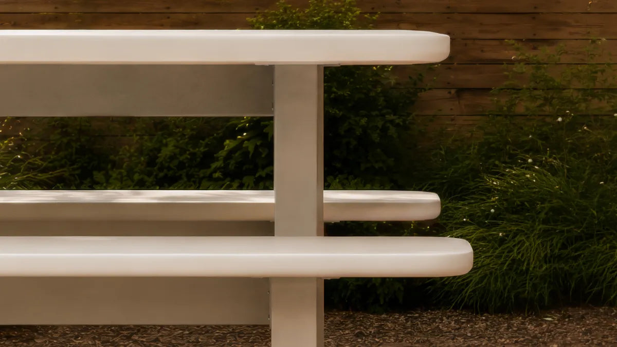 Massif dining table edge and integrated bench in ivory concrete composite, with thick rounded profiles and a slab leg.
