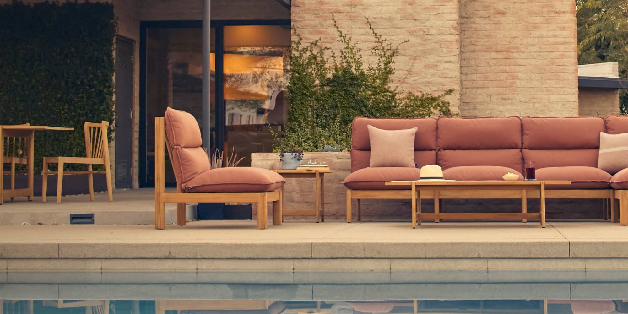 Neighbor Teak sectional with rust-colored cushions with coffee table and chairs on pool deck against a modern home