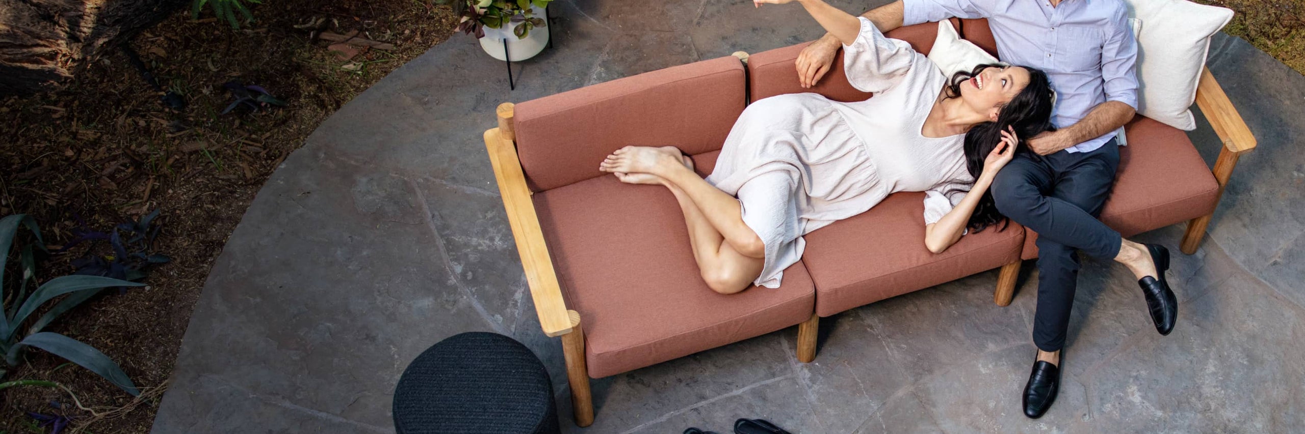 Couple comfortably laying on rust-colored outdoor sofa together