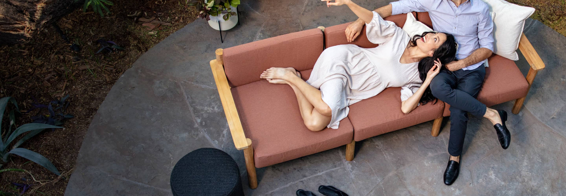 Couple comfortably laying on rust-colored outdoor sofa together