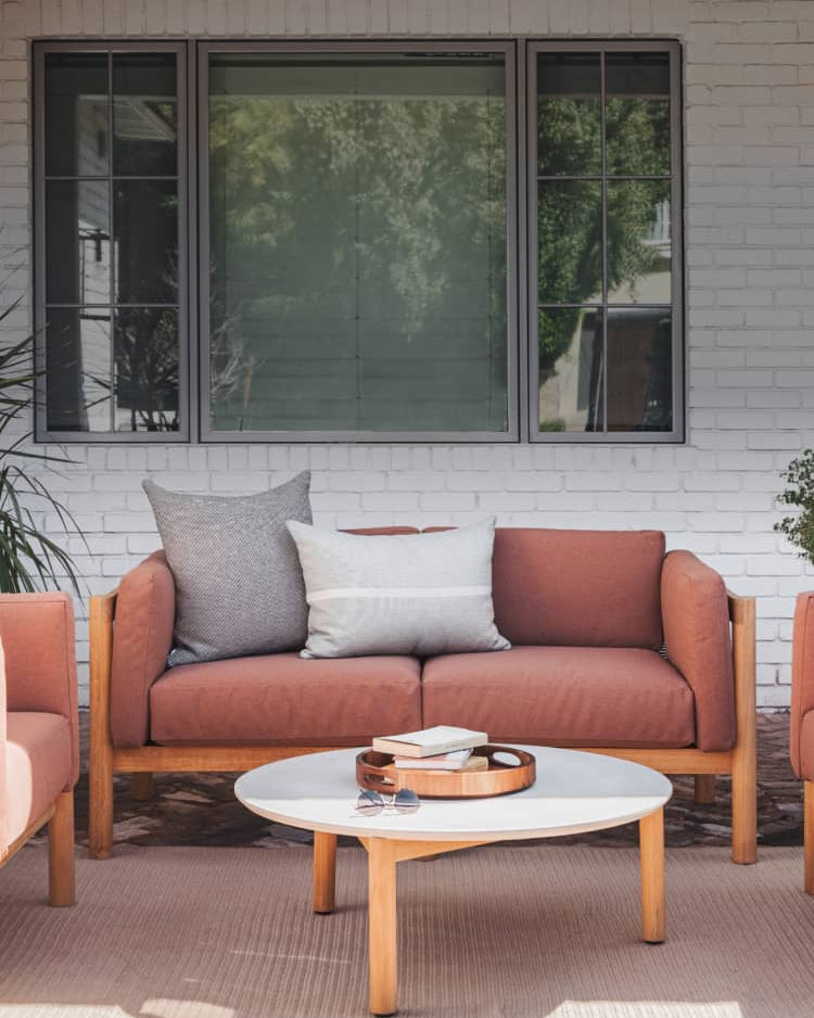 Rust colored cushioned outdoor loveseat made of teak with a concrete table on a brick patio
