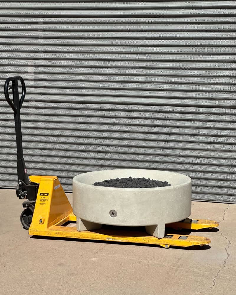 Round concrete fire bowl filled with lava rocks resting on a yellow pallet jack in a warehouse