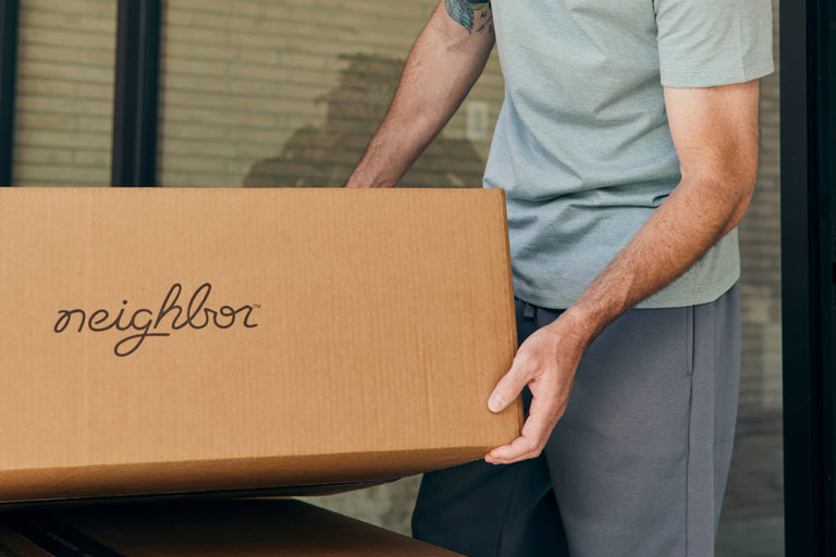 Person carrying a -branded cardboard box through a doorway
