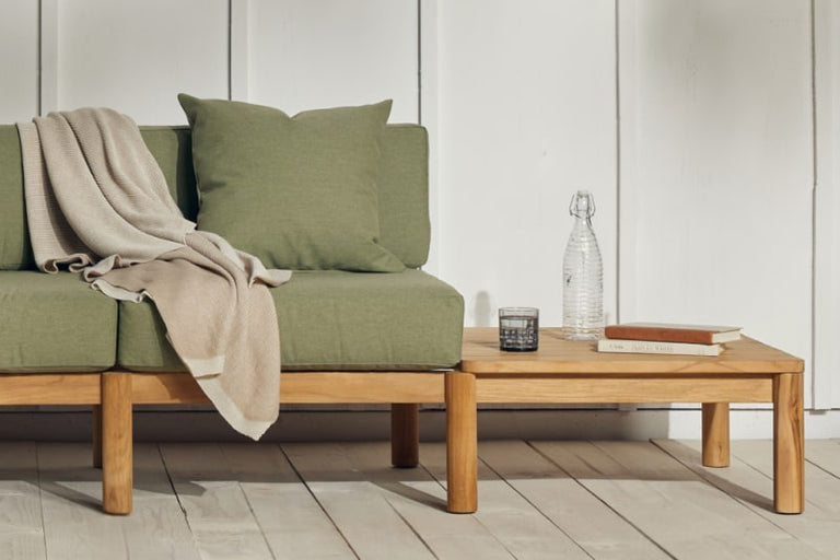 Built-in teak side table that's part of a teak sofa with green cushions. There are books and refreshments placed on the table.