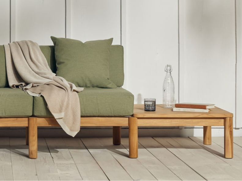 Built-in teak side table that's part of a teak sofa with green cushions. There are books and refreshments placed on the table.