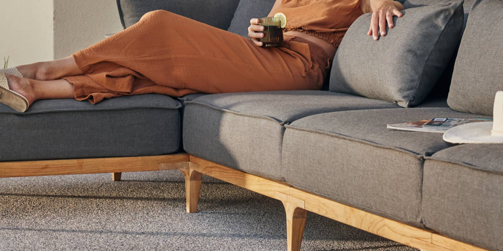 Woman laying on outdoor teak sofa with her legs propped up on an ottoman