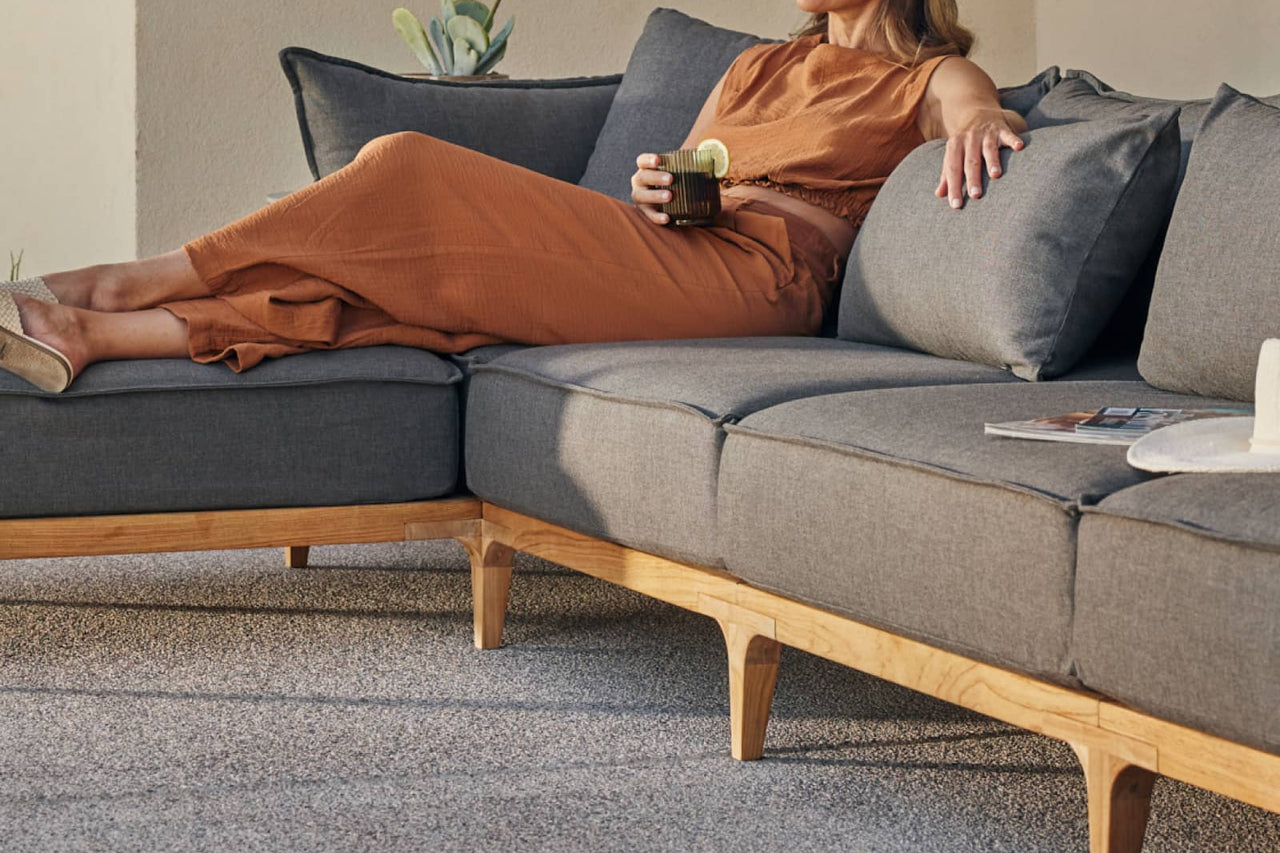 Woman laying on outdoor teak sofa with her legs propped up on an ottoman