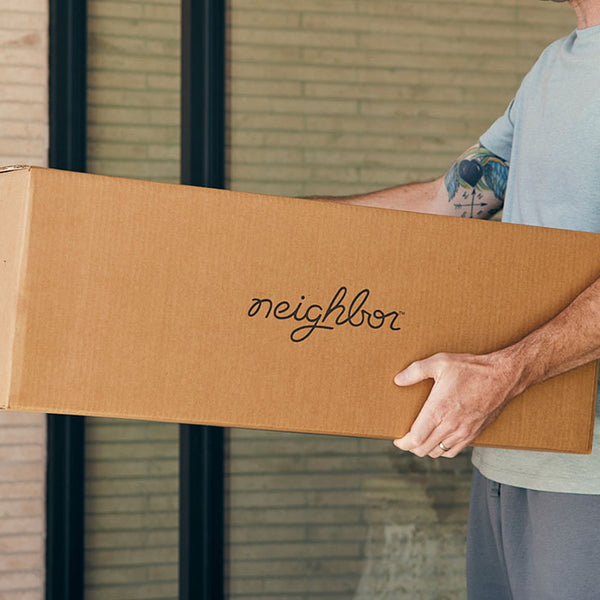 Man carrying a Neighbor-branded cardboard shipping box near a brick building