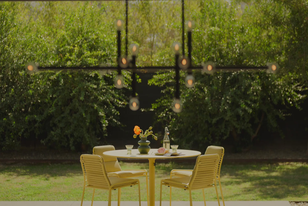 Video of a yellow dining table with four matching chairs and seat pads. Specific focus on the Neighbor XY Dining Chair, a yellow, metal dining chair with a Sunbrella, yellow seat pad. 