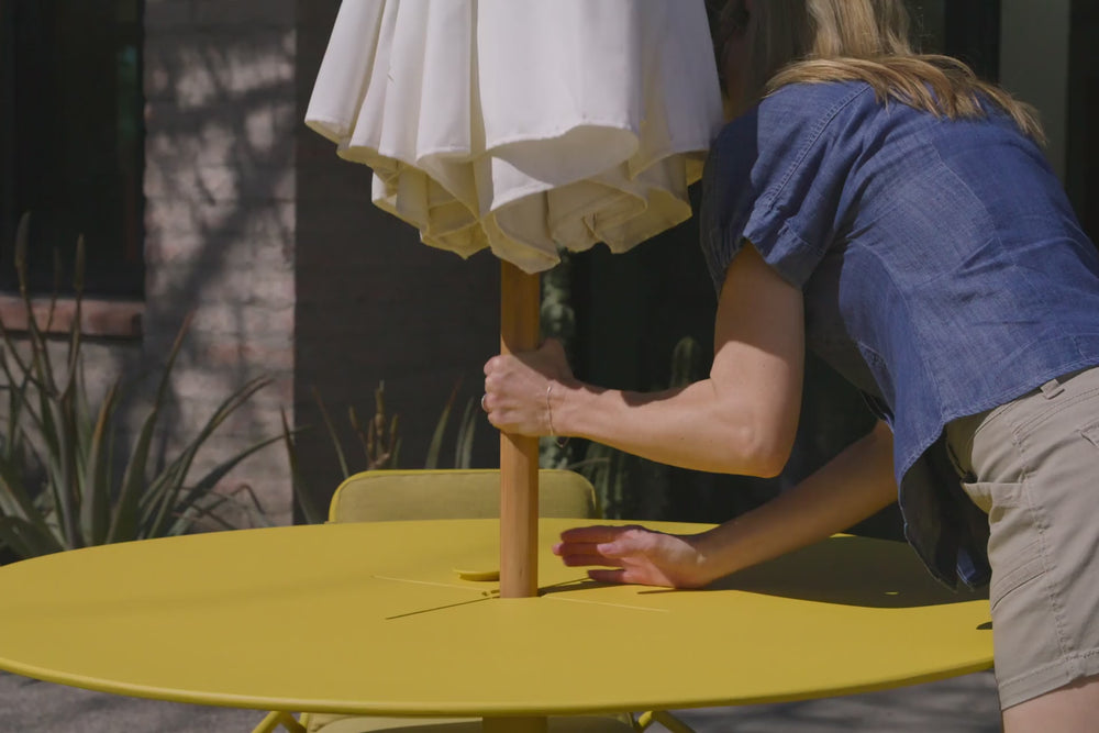 Video of a yellow dining table with four matching chairs and seat pads. Specific focus on the Neighbor XY Dining Table, a yellow, metal dining table with integrated umbrella holder. 