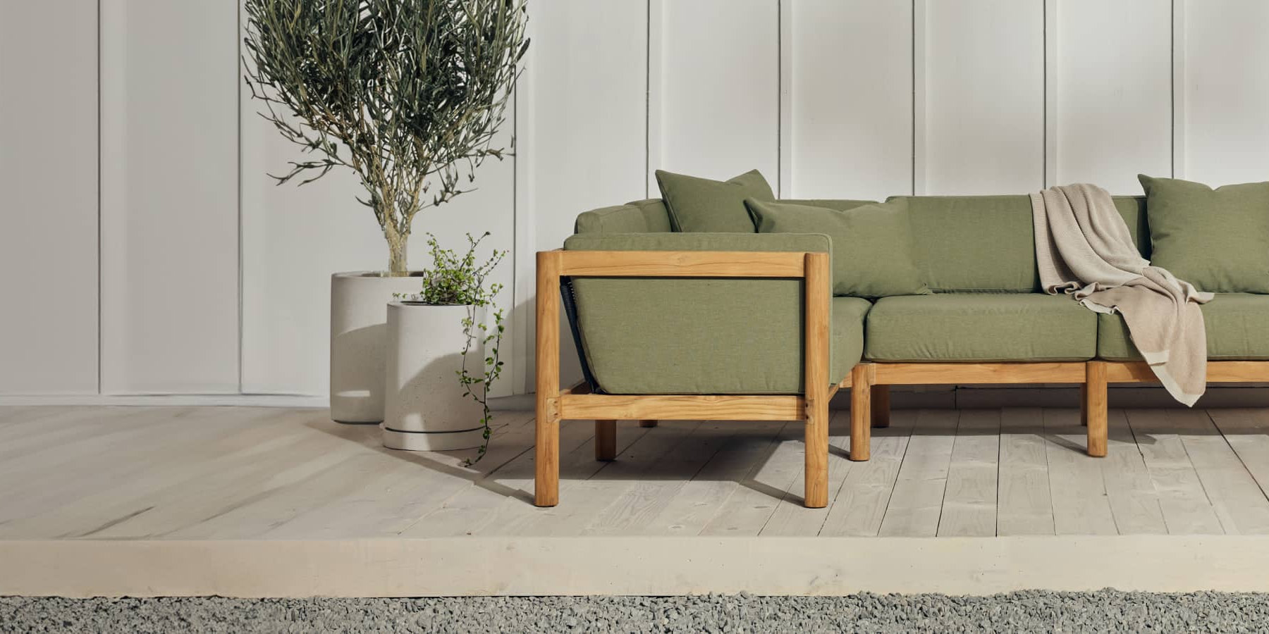 Neighbor teak outdoor sectional with an end table on a patio with a potted olive tree